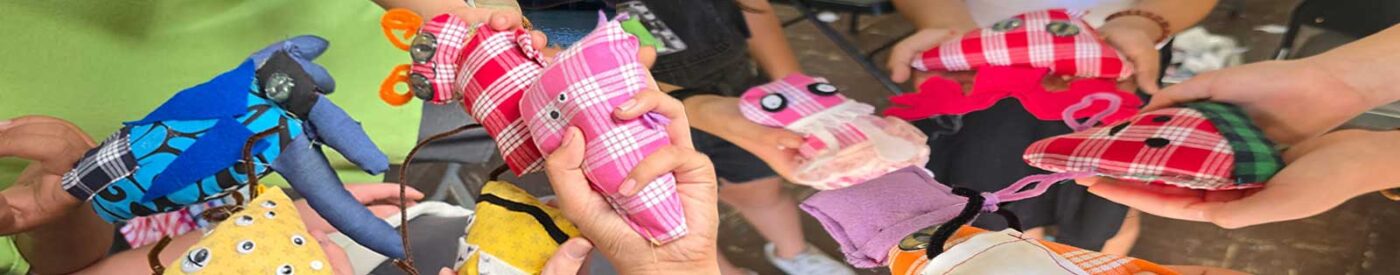 Children proudly holding colorful handmade monsters sewn from palaka fabric during a keiki art workshop in Hilo, Hawaiʻi.